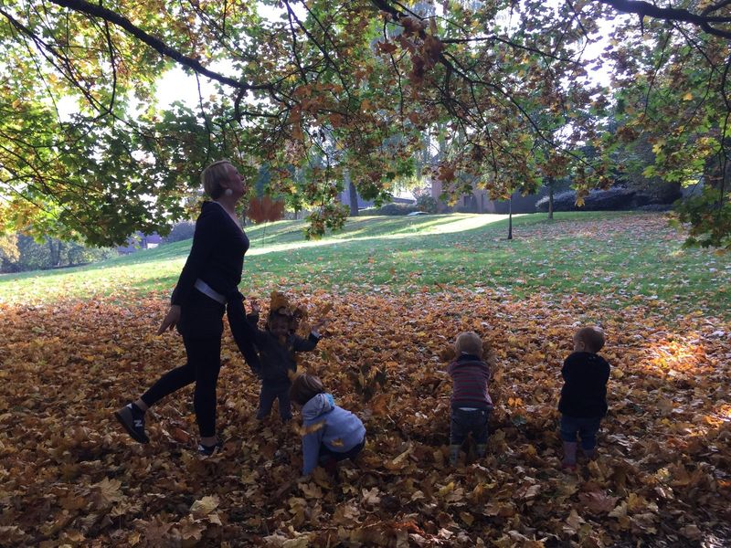 Des enfants jouent dans les feuilles d'automne avec une puéricultrice